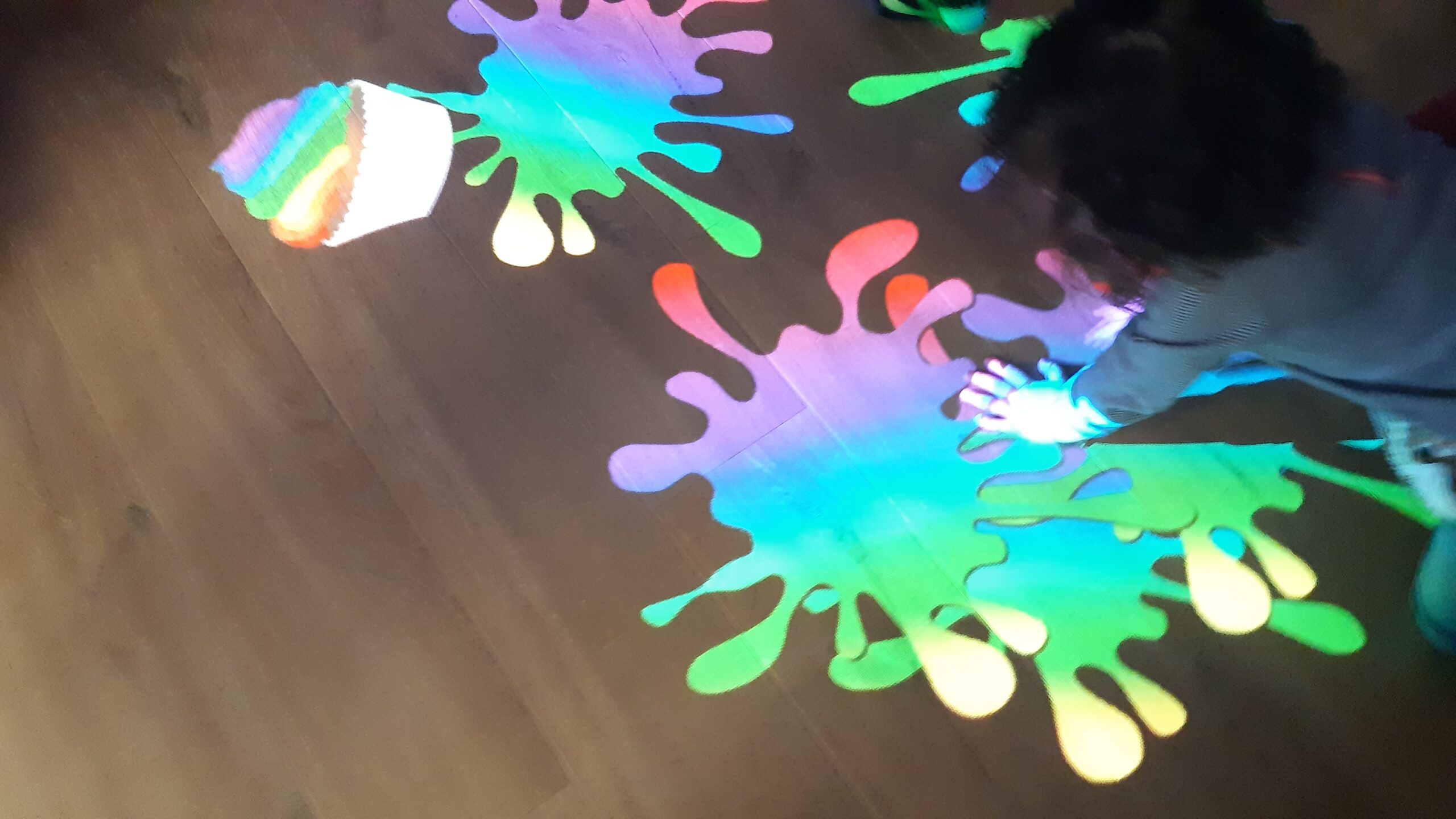 Pre-school child playing with interactive projector (projecting colourful paint splashes on floor)